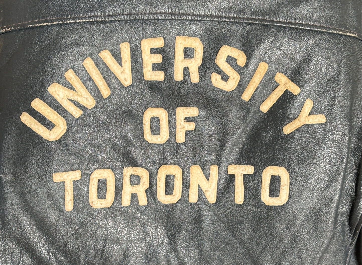 Black leather jacket with 'University of Toronto' text in gold on a dark background