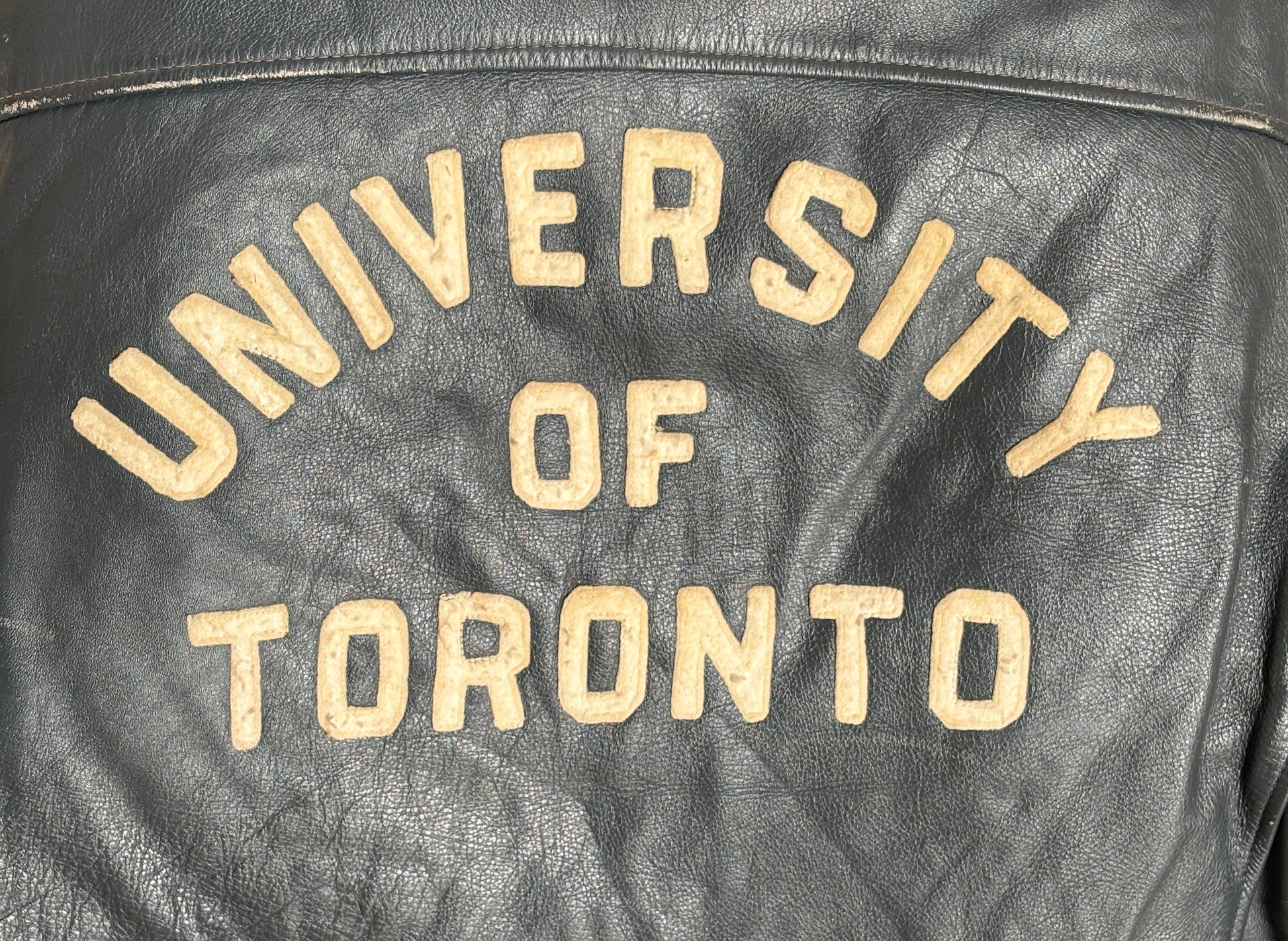 Black leather jacket with 'University of Toronto' text in gold on a dark background