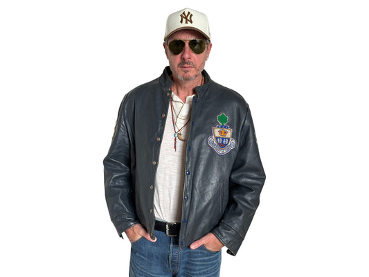 Man wearing a leather jacket with a logo, sunglasses, and a cap on a white background