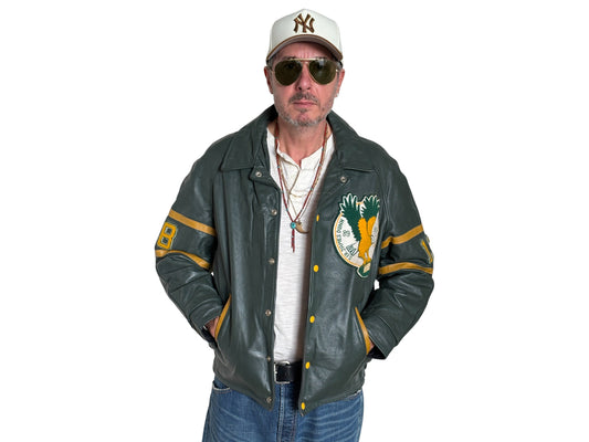 Man wearing a green varsity jacket with a logo, sunglasses, and a cap on a white background