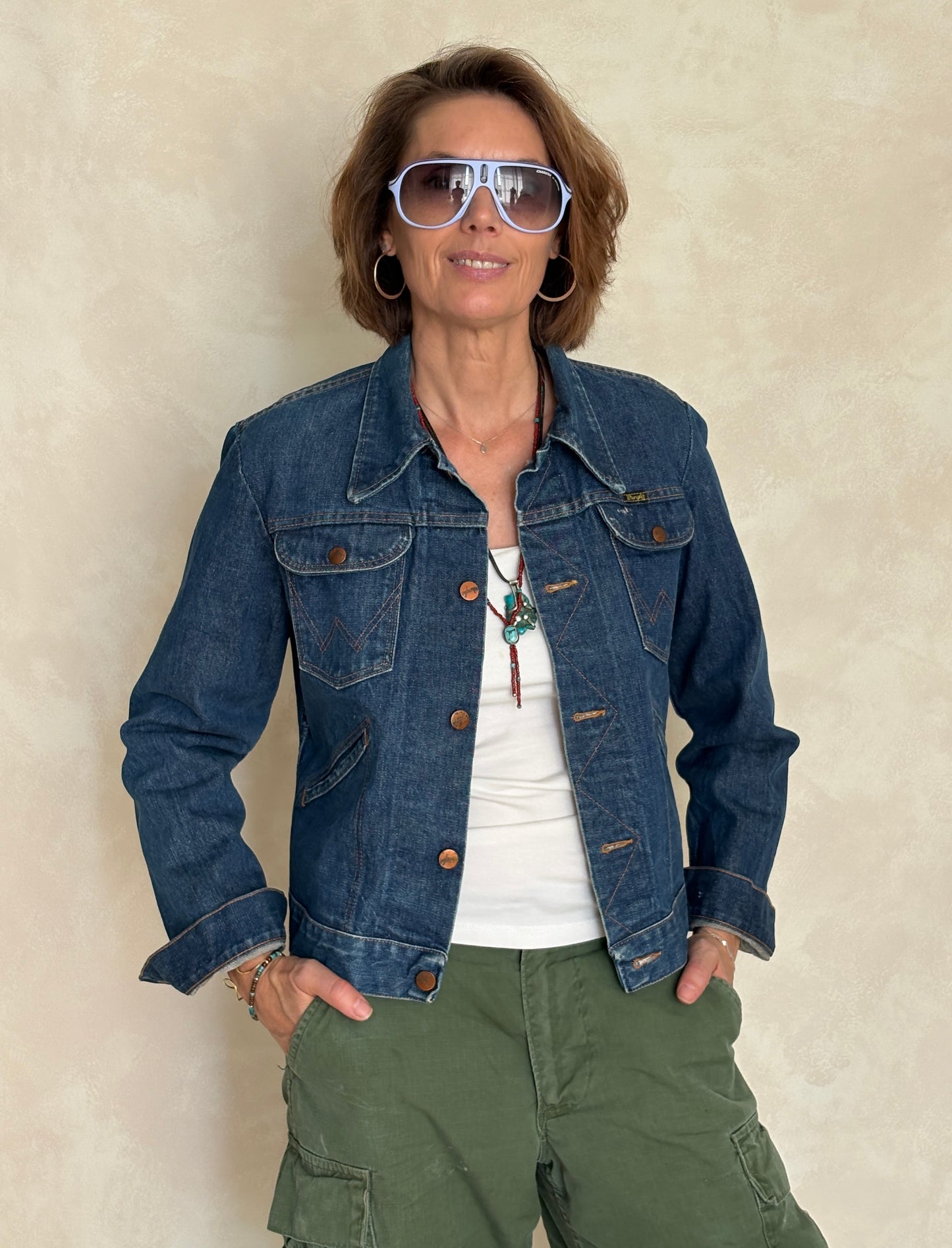Woman wearing a denim jacket and sunglasses against a beige background